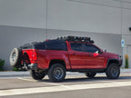 Red pickup truck with off-road equipment parked in front of a gray building.