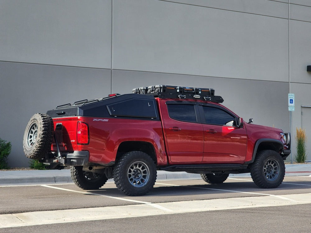 Red pickup truck with off-road equipment parked in front of a gray building.