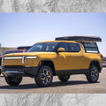 Yellow electric pickup truck with a camper shell on a clear day.