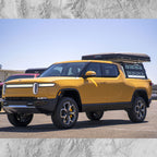 Yellow electric pickup truck with a camper shell on a clear day.